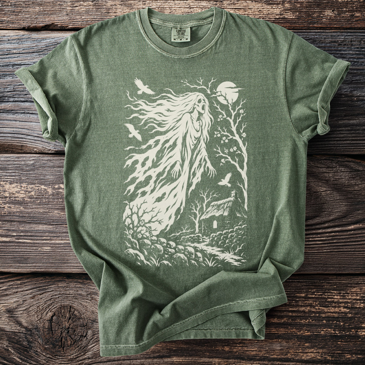 Green t-shirt with a white graphic of a ghostly figure, birds, trees, and a cottage.