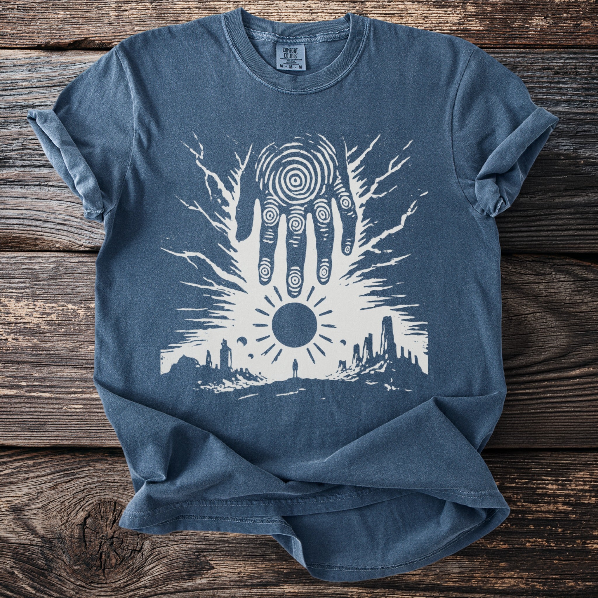 Blue t-shirt with a white graphic of a hand, sun, and desert landscape.