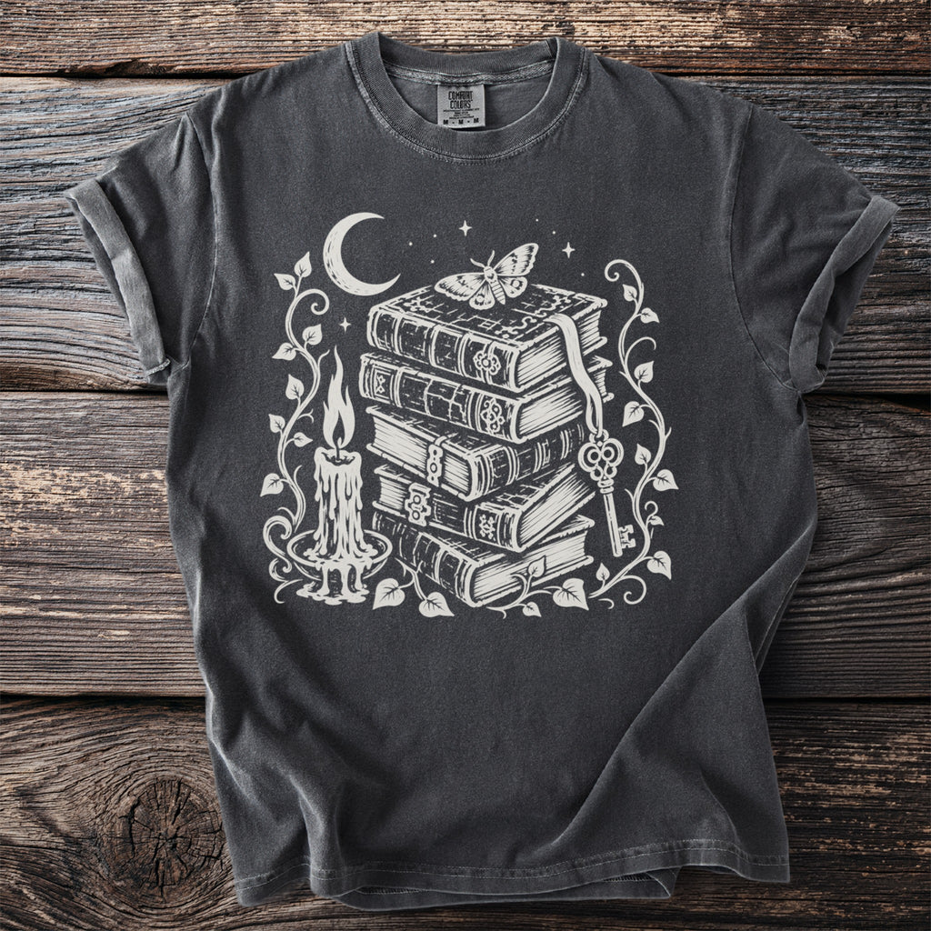 Dark grey t-shirt with white print of stacked books, candle, moth, moon, and key.