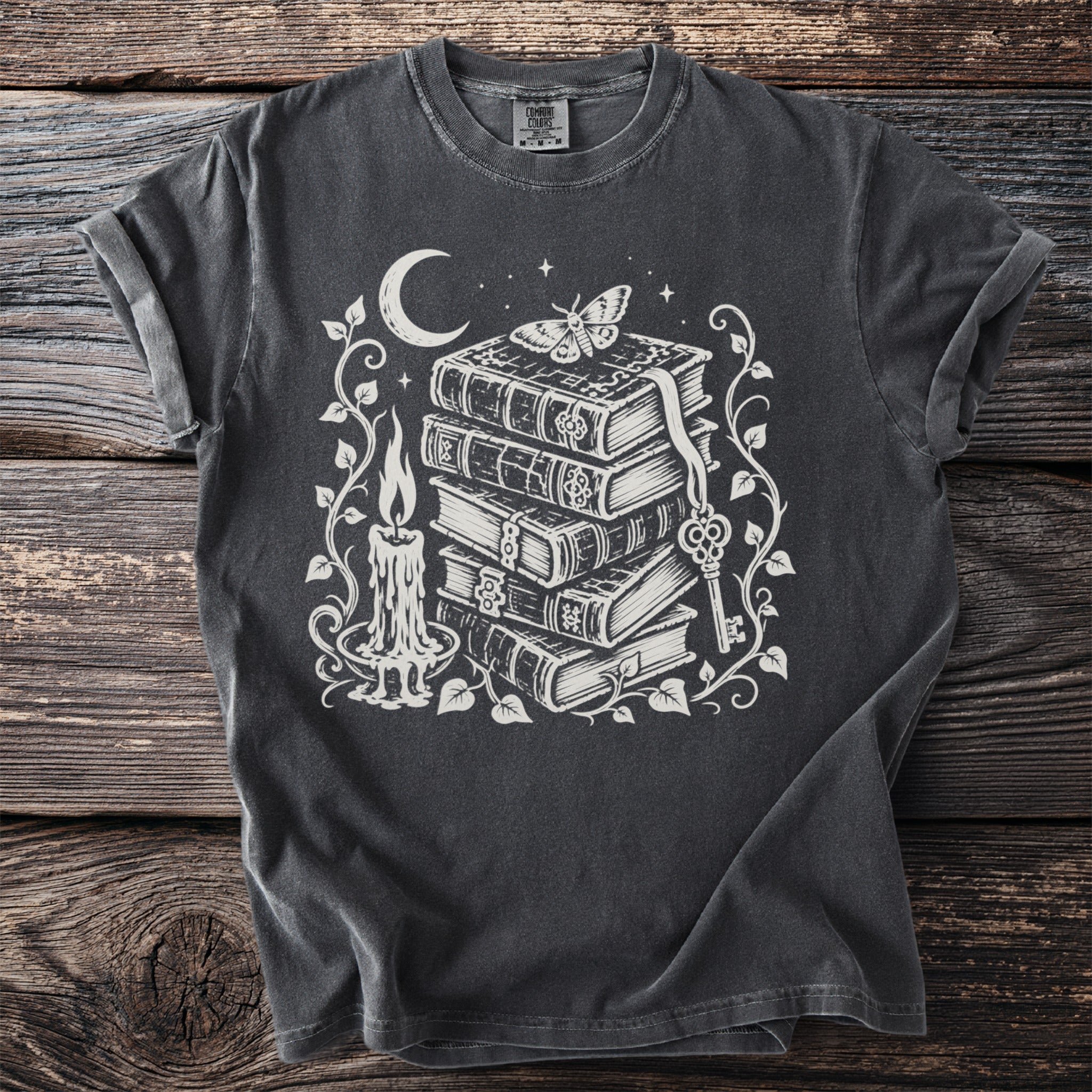 Dark grey t-shirt with white print of stacked books, candle, moth, moon, and key.