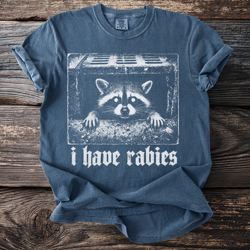 T-shirt with raccoon peeking over sewer grate and text "i have rabies".