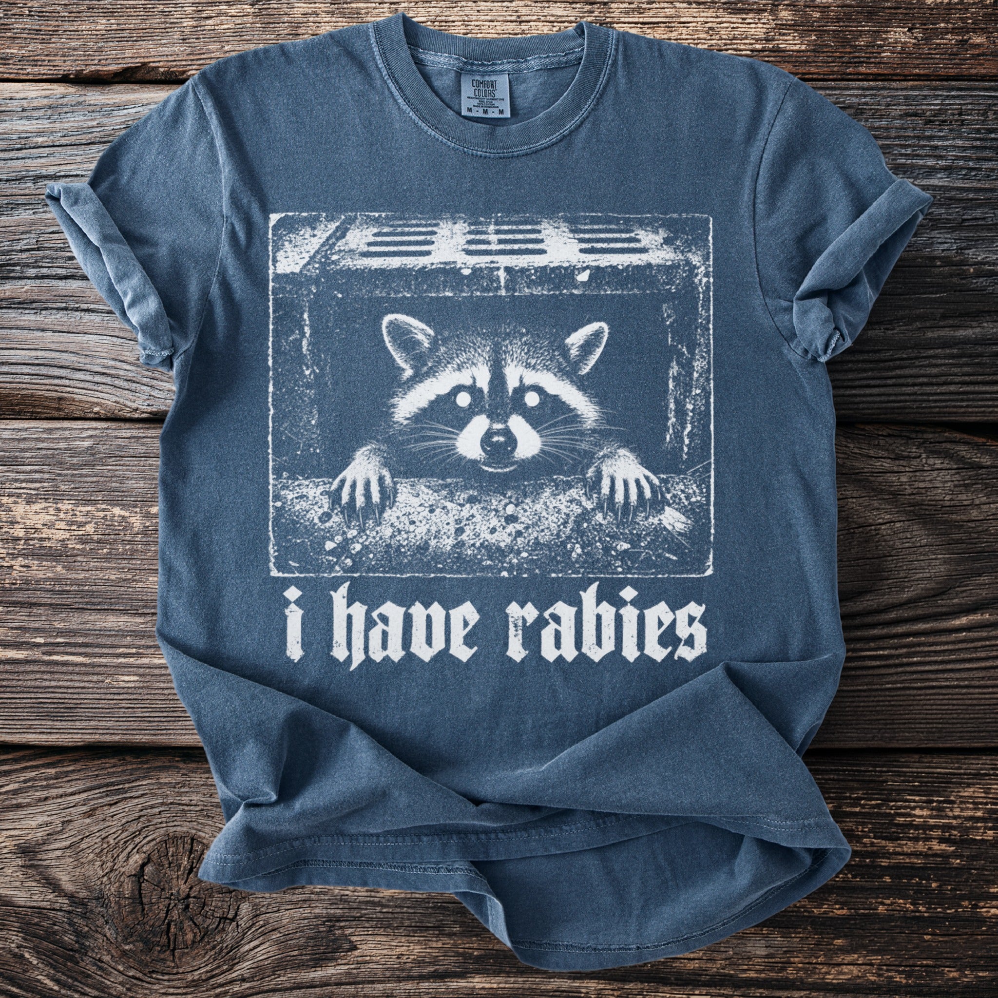 T-shirt with raccoon peeking over sewer grate and text "i have rabies".