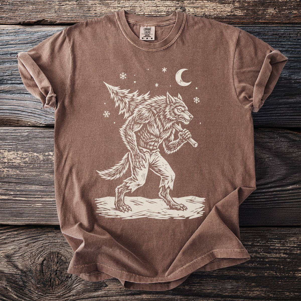 Espresso brown t-shirt with a cream folk-cut print: a snarling werewolf in torn trousers walks through the snow with a fir tree over his shoulder.