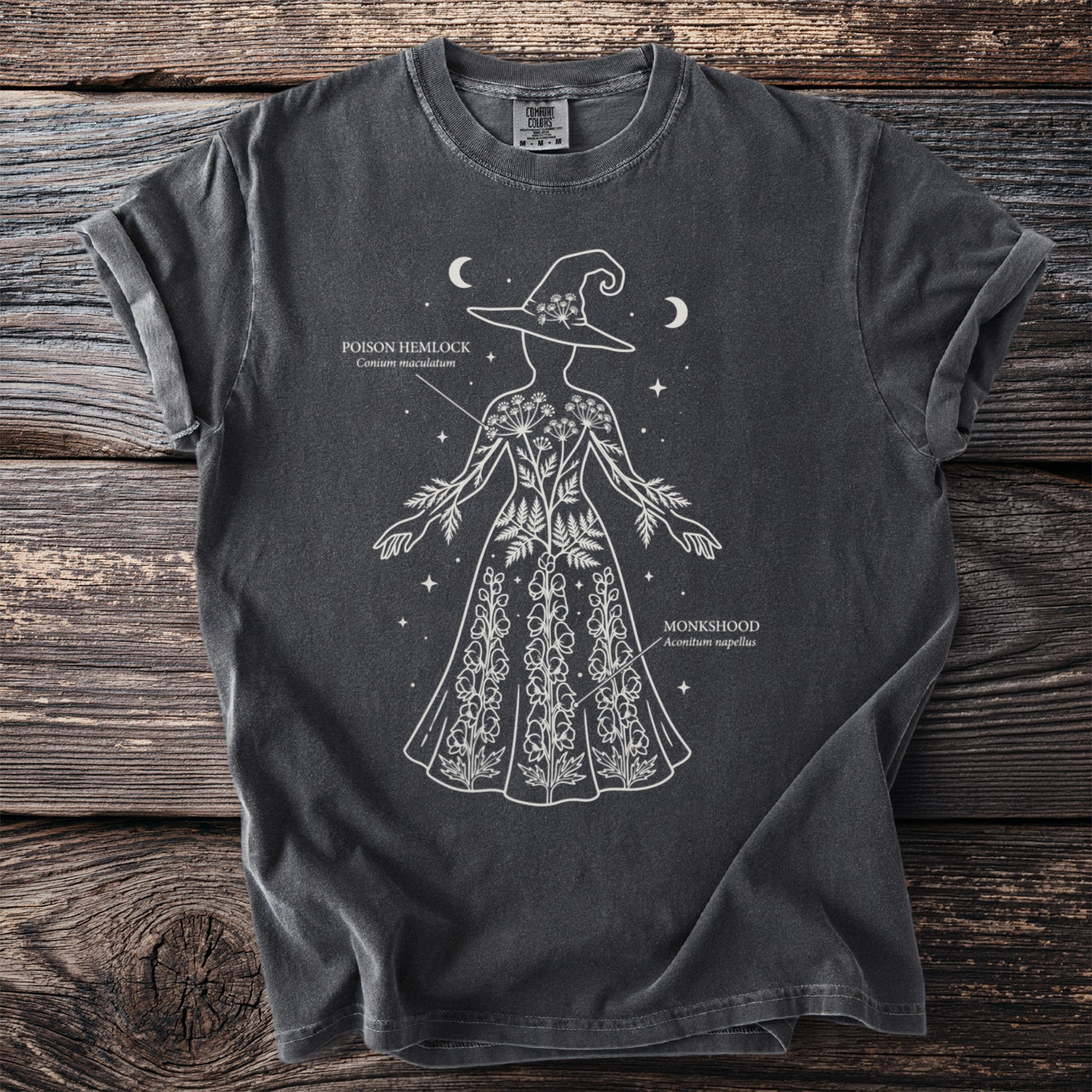 Dark t-shirt with white line art of a woman wearing a witch hat and adorned with poison hemlock and monkshood.