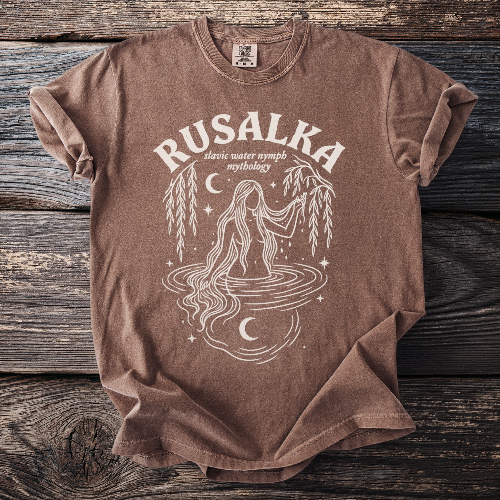 Brown t-shirt with white graphic of a Rusalka and "Slavic water nymph mythology".