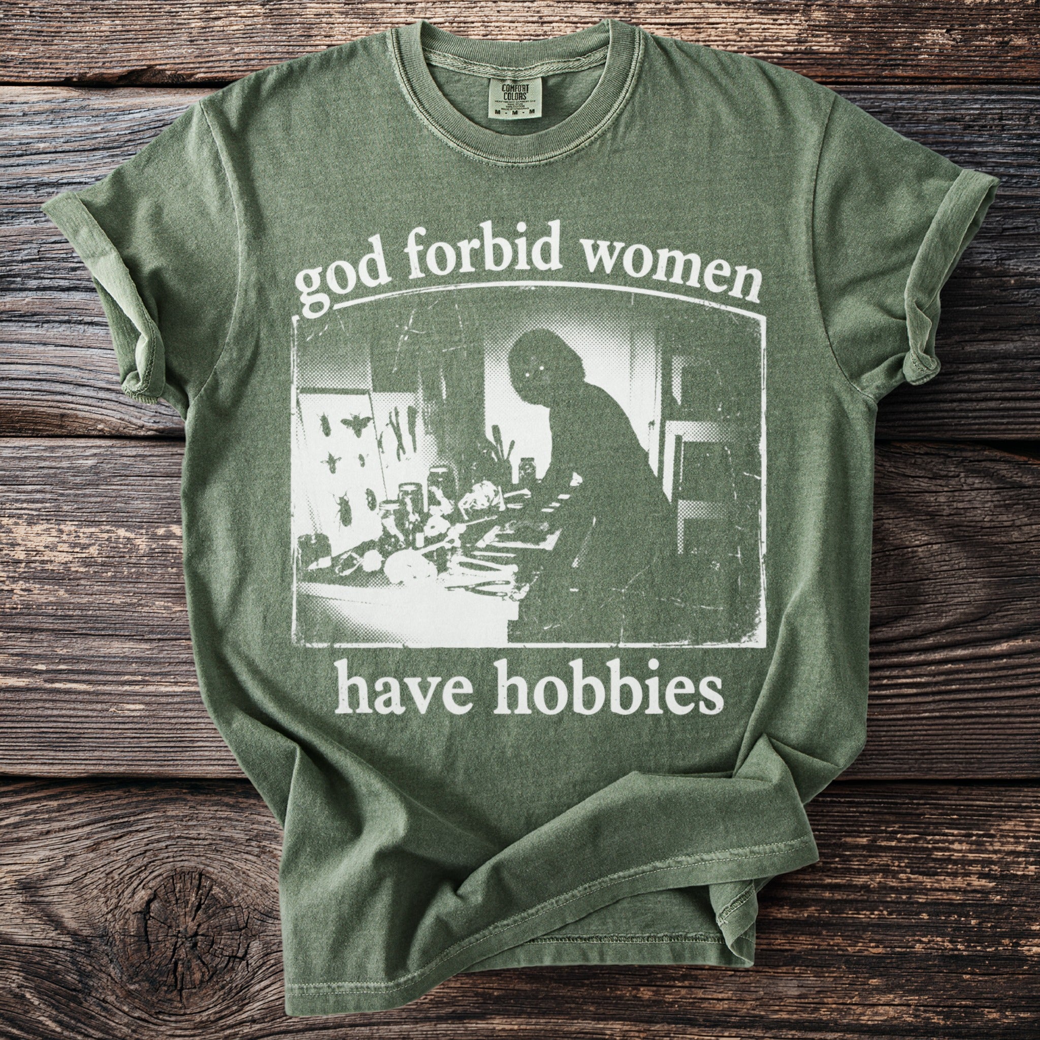 Green t-shirt with text "god forbid women have hobbies" and a silhouette.