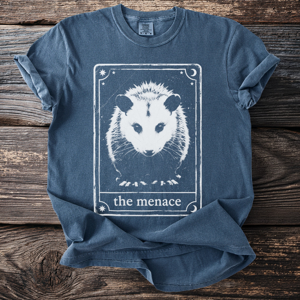Blue t-shirt with opossum graphic and text "the menace" in a tarot card design.