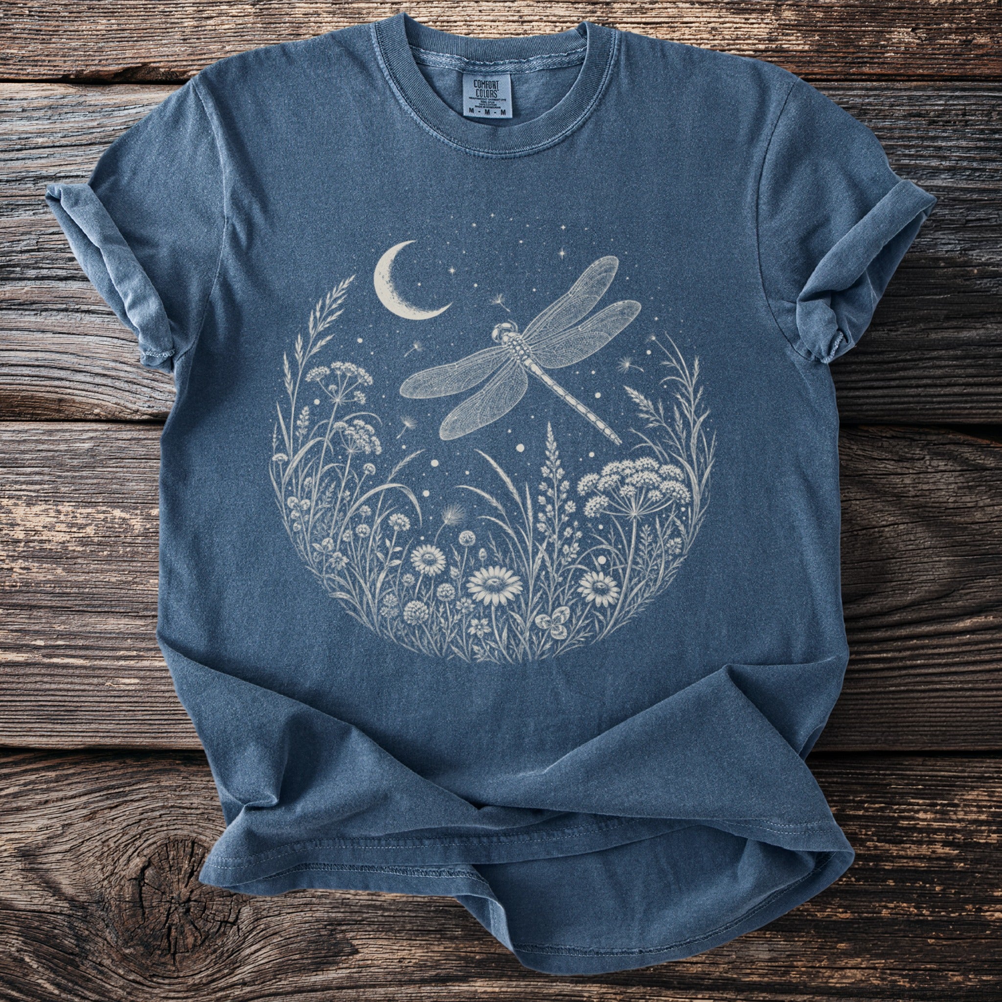 Blue t-shirt with a circular print of a dragonfly among flowers, moon, and stars.