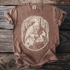 Brown t-shirt with a cream graphic of a witch stirring a cauldron with a raven.