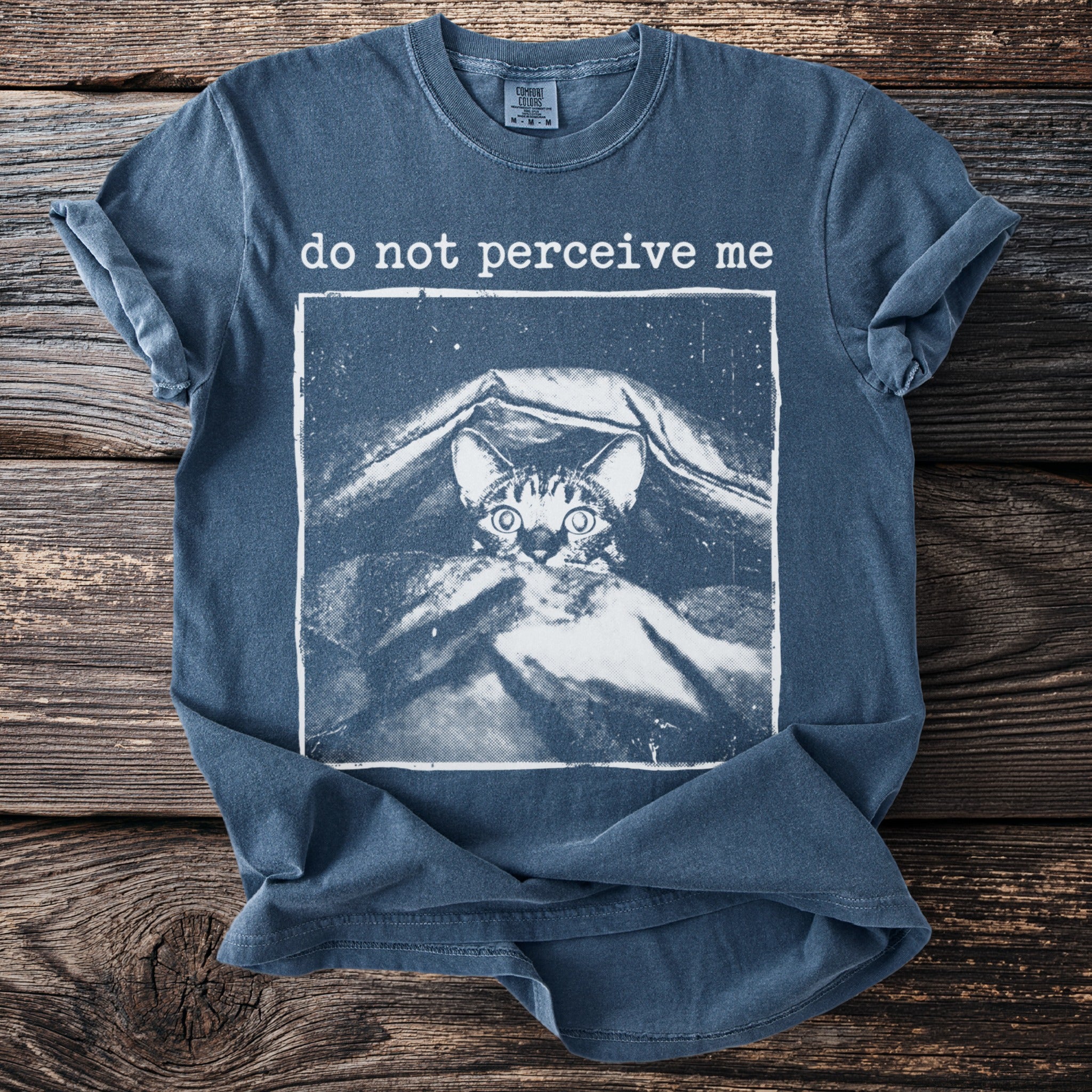 Blue t-shirt with a cat peeking out from under a blanket and the text "do not perceive me".