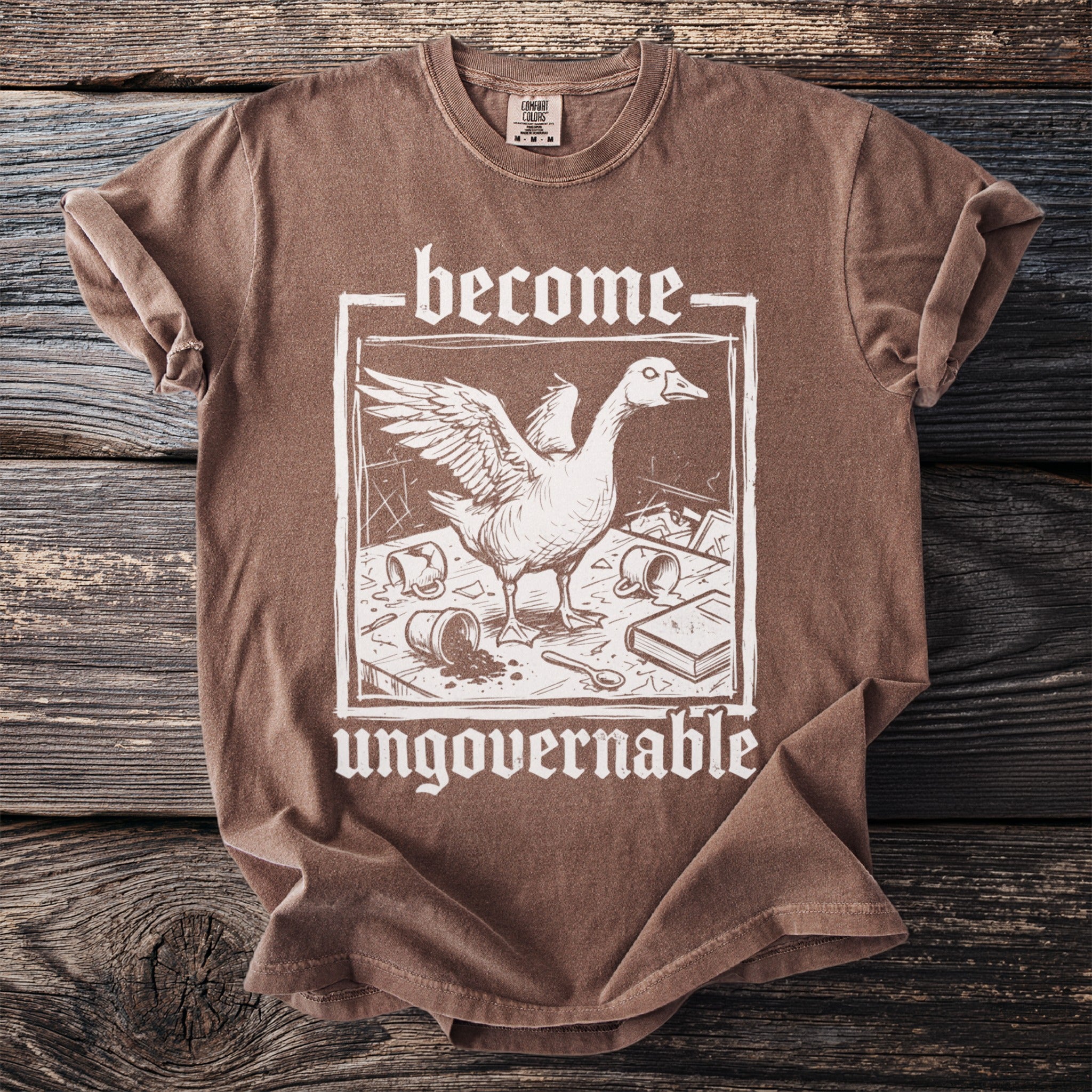 Brown t-shirt with white text "become ungovernable" and goose illustration.