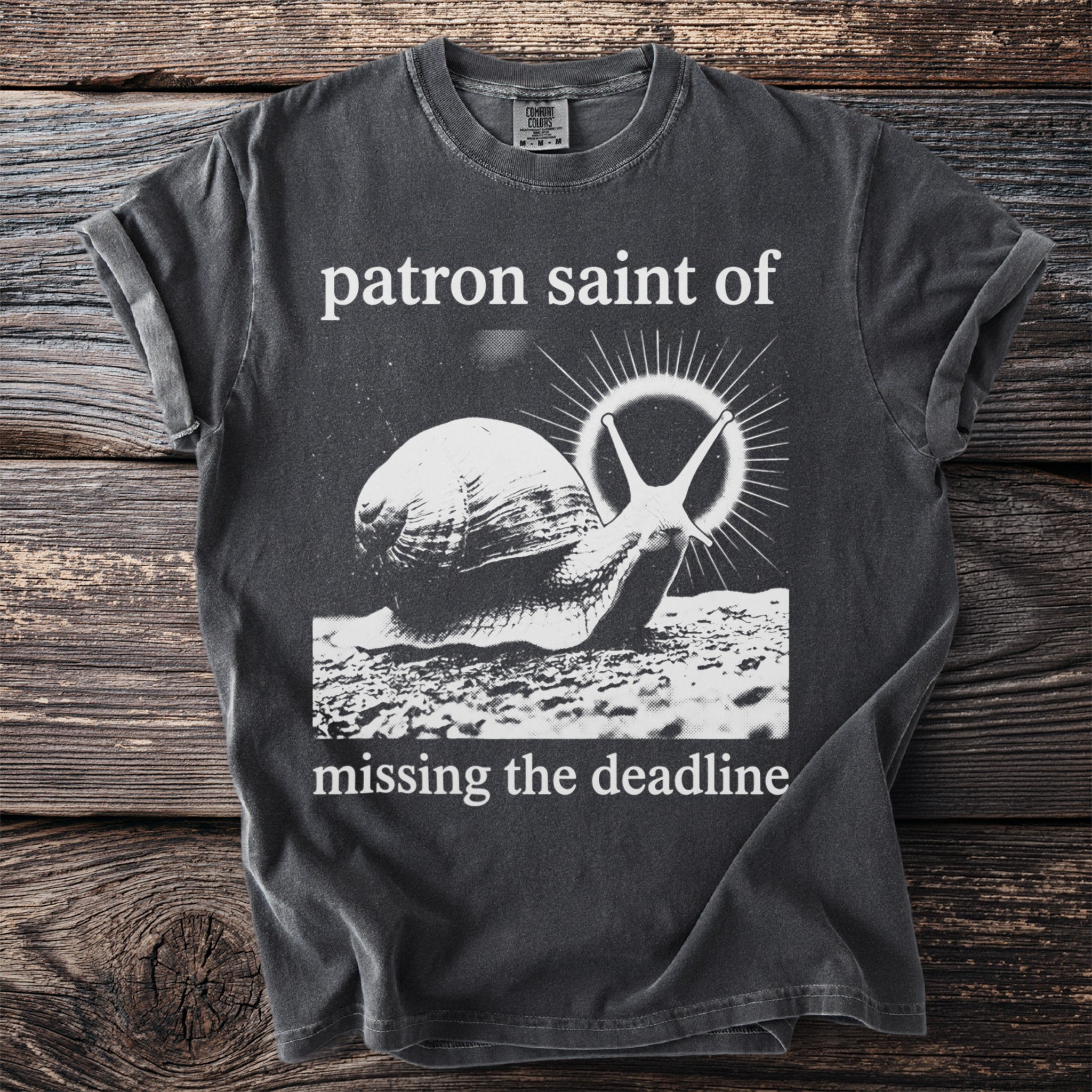 Dark gray t-shirt with a snail and text: Patron saint of missing the deadline.