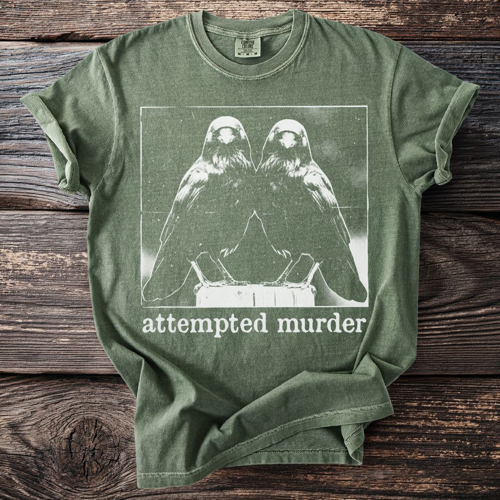 Green t-shirt with a white graphic of two crows and the text "attempted murder".