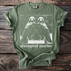 Green t-shirt with a white graphic of two crows and the text "attempted murder".