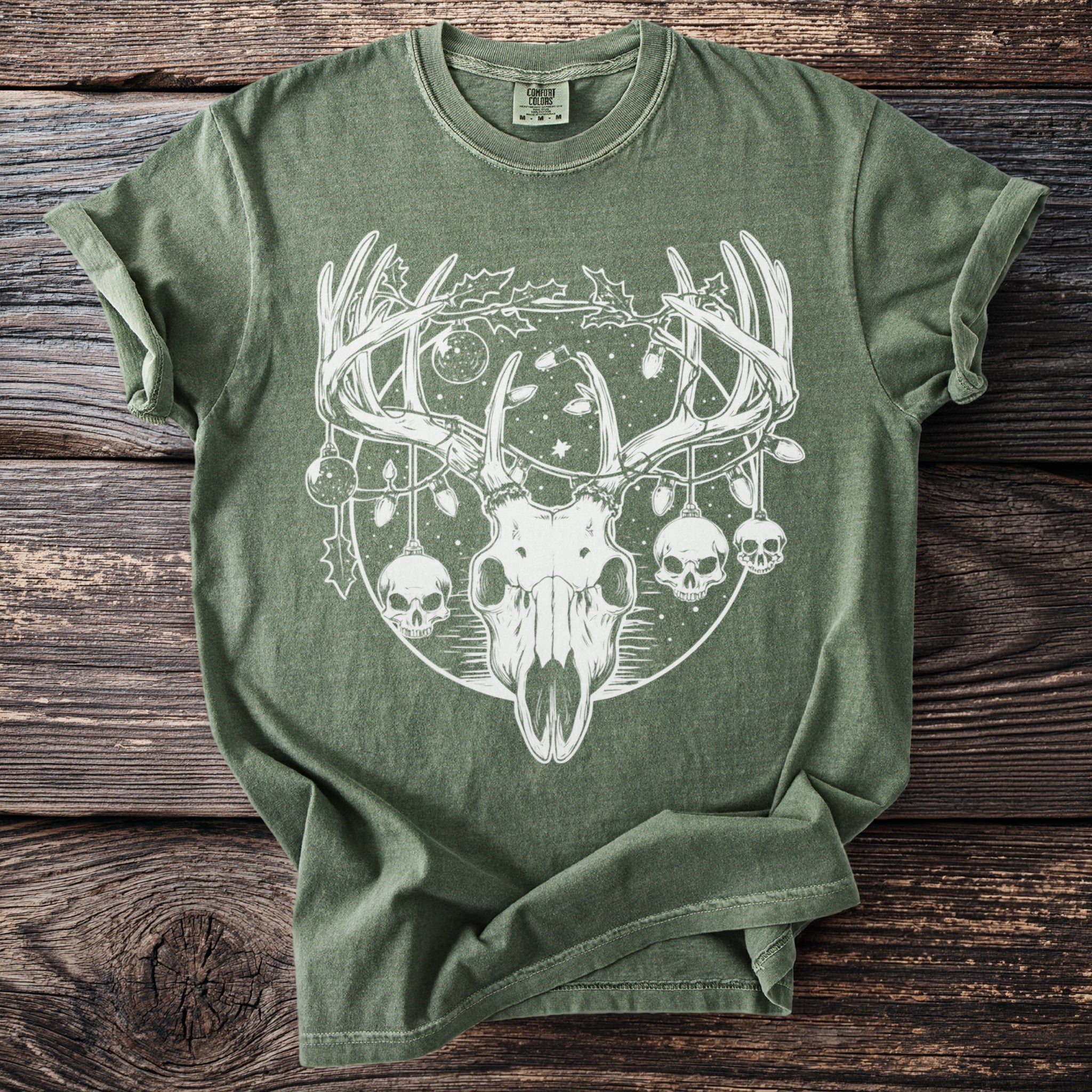 Green t-shirt with white graphic of deer skull, holly, ornaments, and skulls.