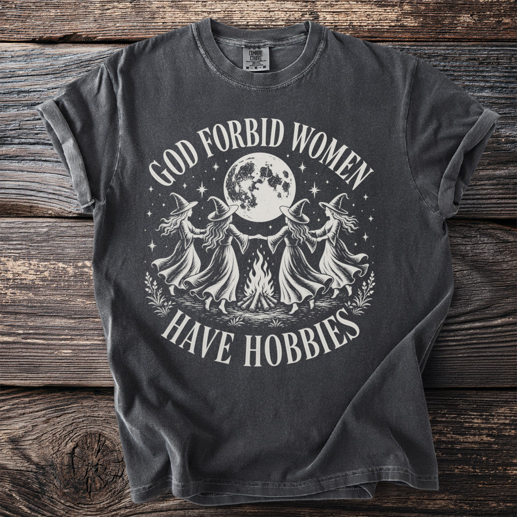 Dark grey t-shirt with women dancing under a moon, reading "God Forbid Women Have Hobbies".