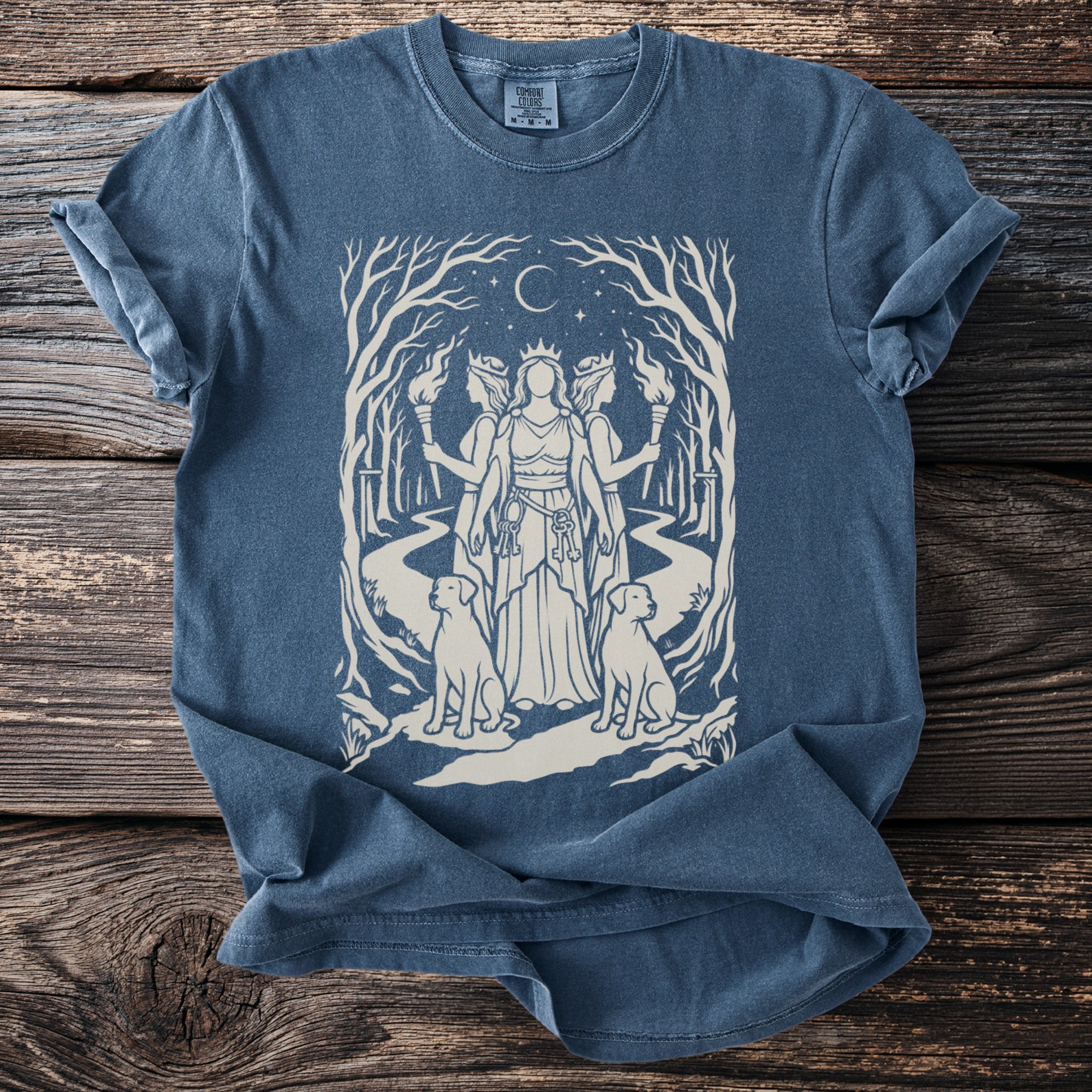 Blue shirt with a cream graphic of a three-headed woman, dogs, torches, and trees.