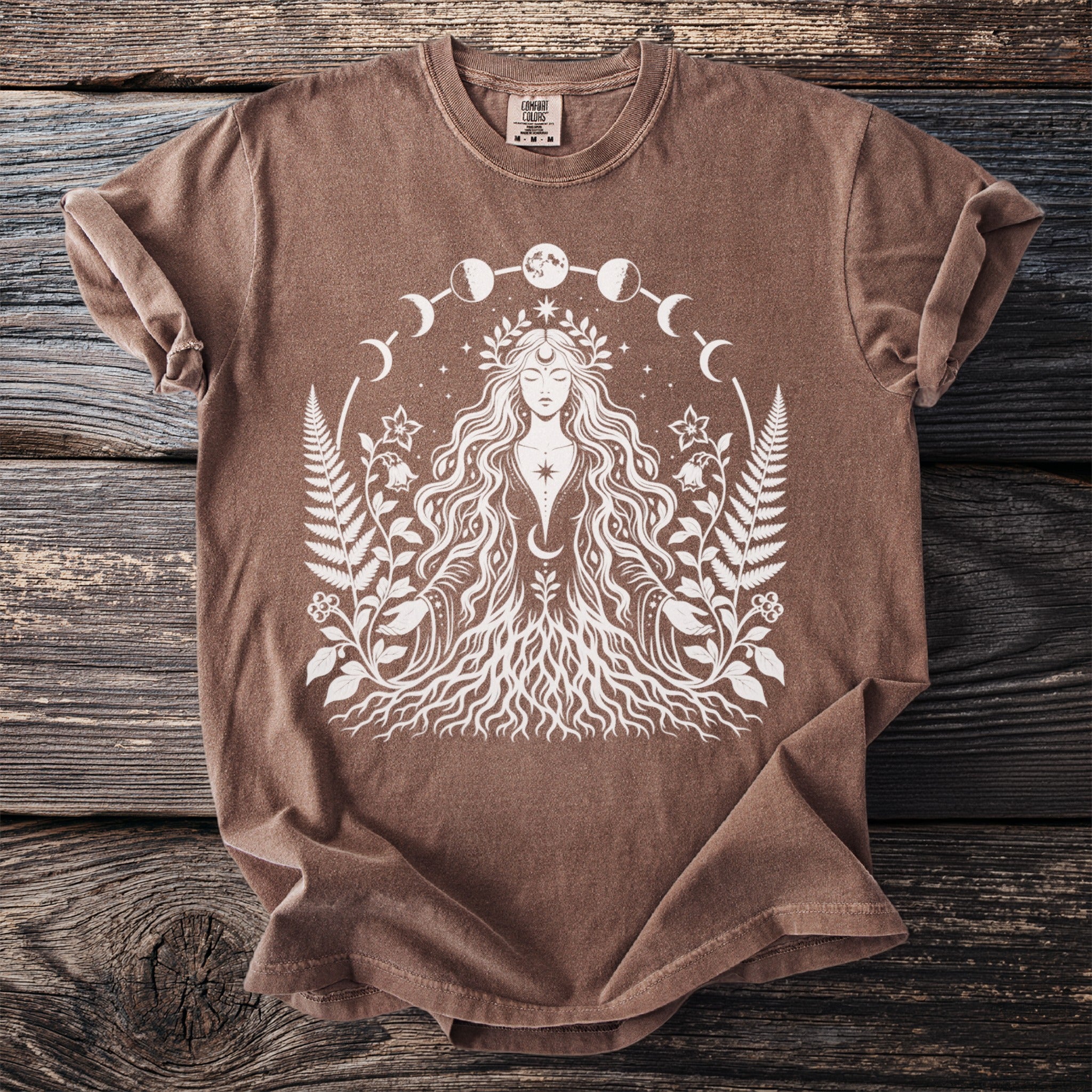 Brown t-shirt with white design of woman with roots, ferns, moon phases, and stars.