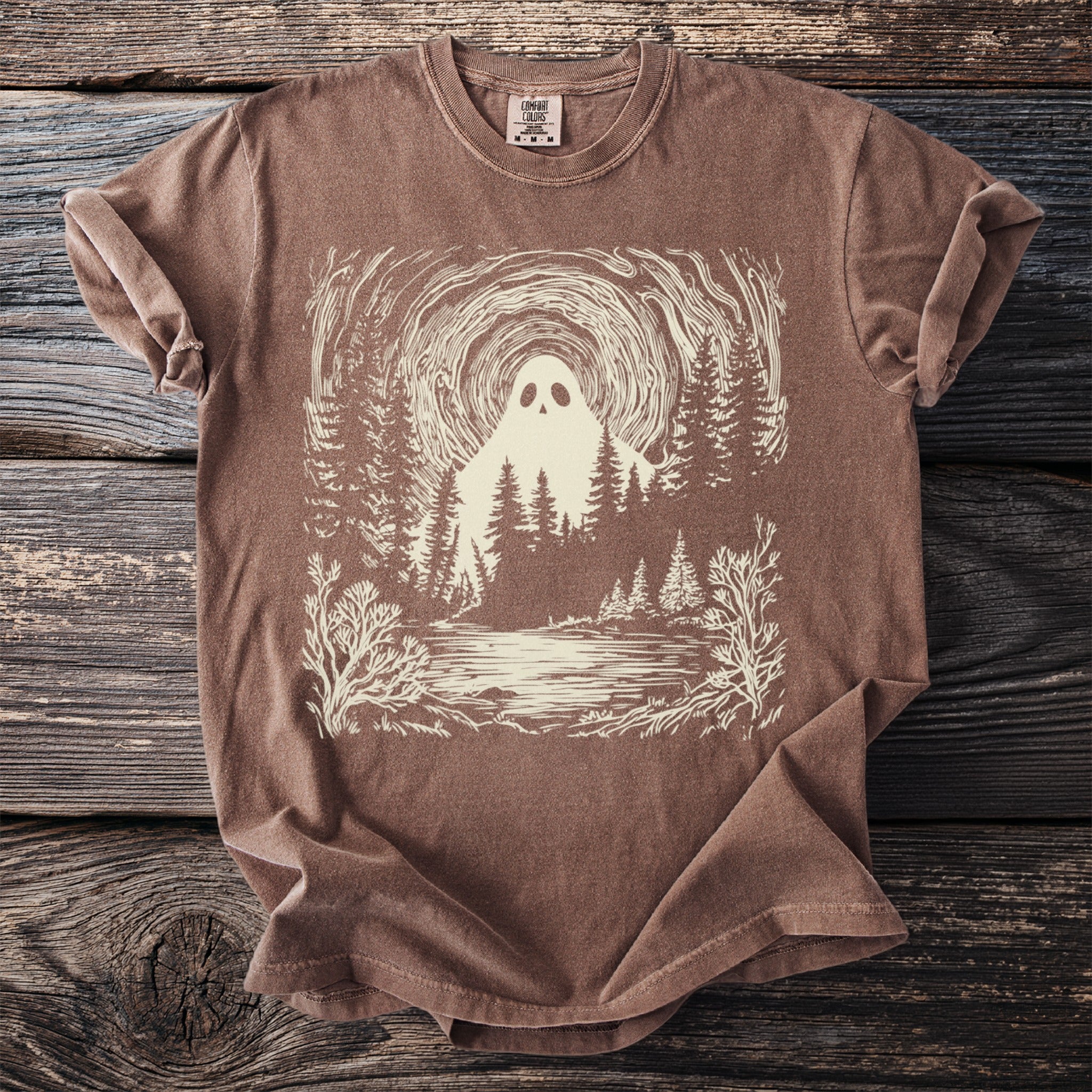 Brown t-shirt with a cream graphic of a ghost in a forest by a lake.