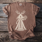 Brown Comfort Colors t-shirt with a cream graphic of a horned figure holding a sun-like symbol.