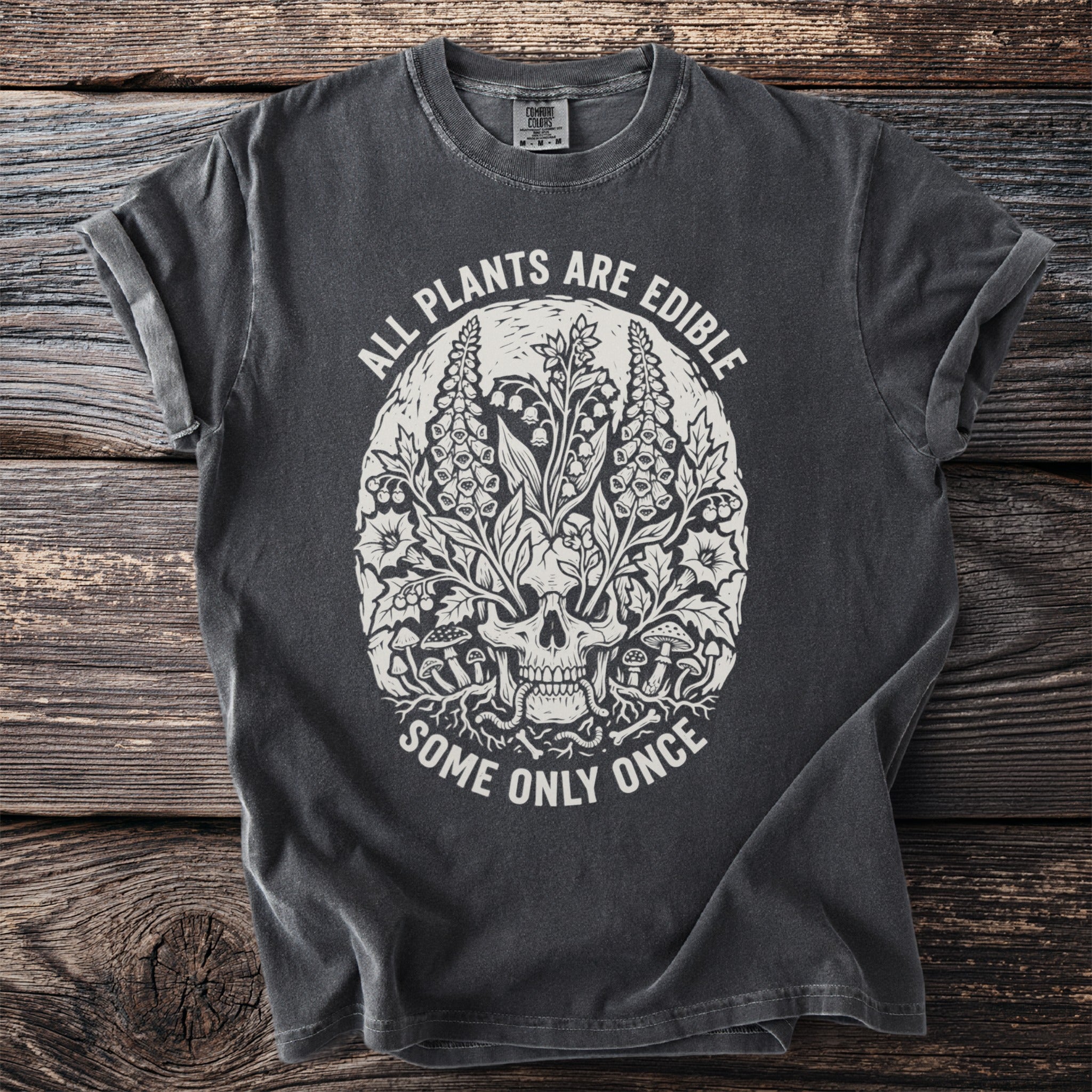 Dark grey t-shirt with skull, plants, and text: "ALL PLANTS ARE EDIBLE SOME ONLY ONCE."