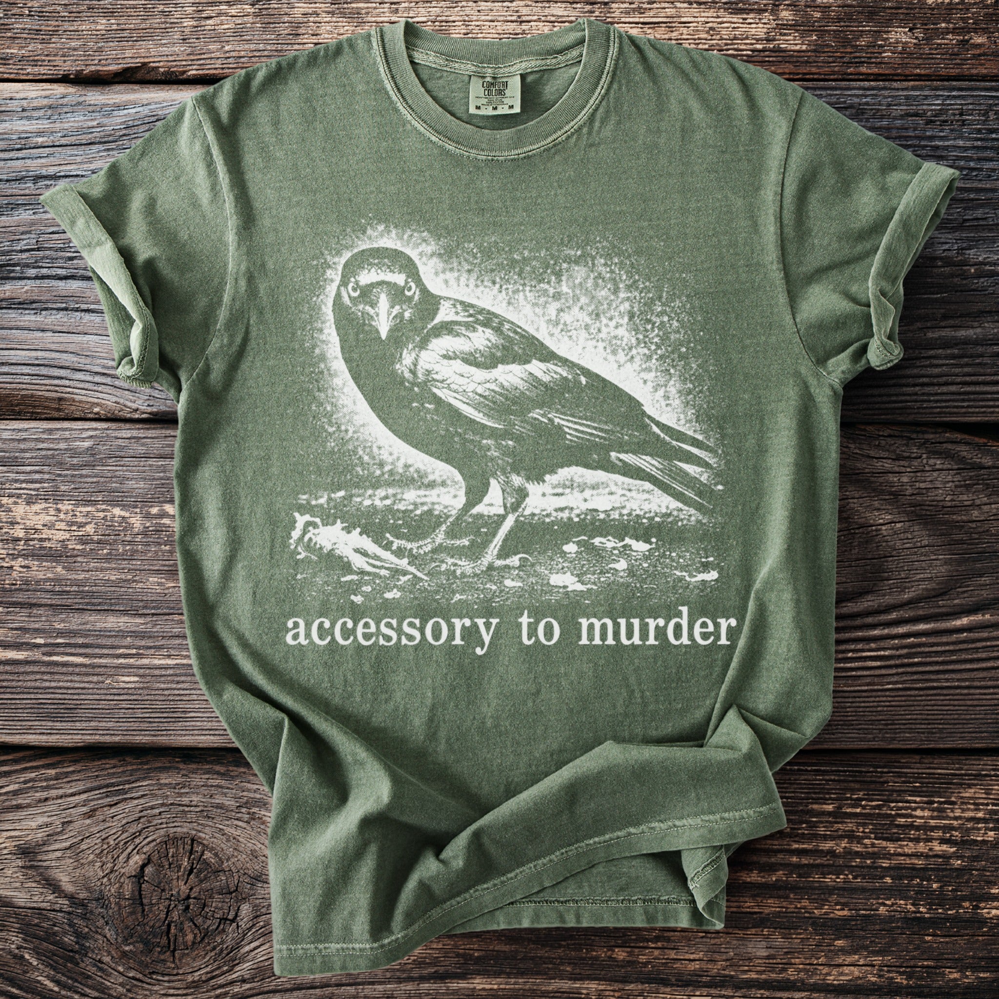 Olive green t-shirt with a crow graphic and text "accessory to murder".