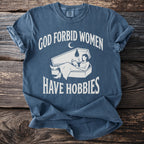 Blue t-shirt with white text "God Forbid Women Have Hobbies" and coffin graphic.