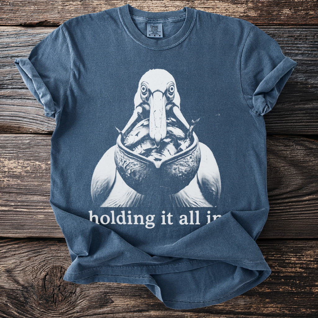 Blue t-shirt with white graphic of pelican holding fish and text "holding it all in."