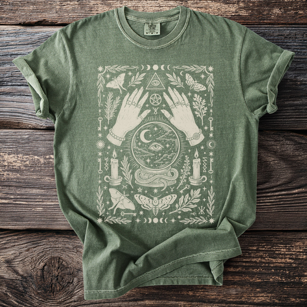 Green t-shirt with mystical design featuring hands, crystal ball, moths, and candles.