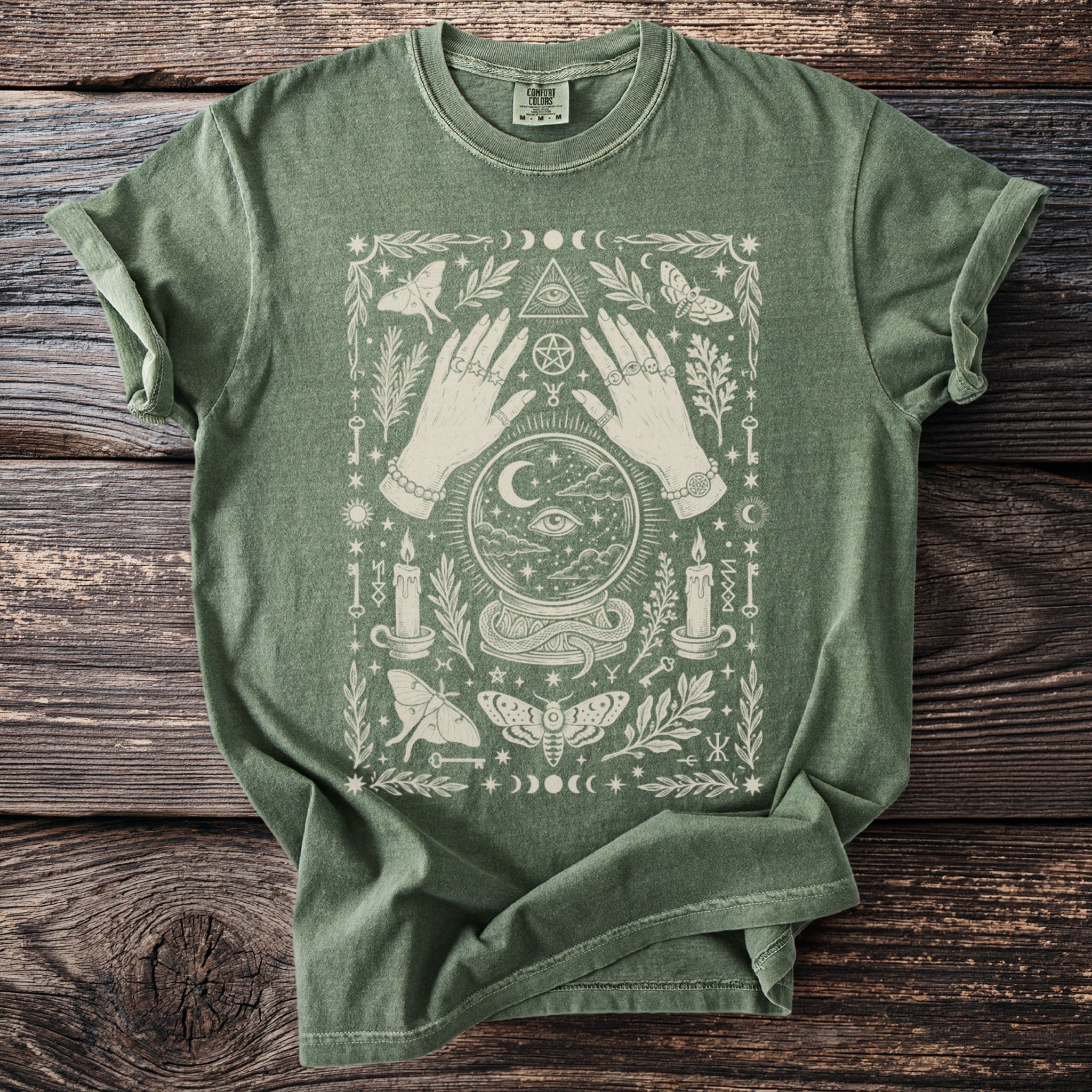 Green t-shirt with mystical design featuring hands, crystal ball, moths, and candles.