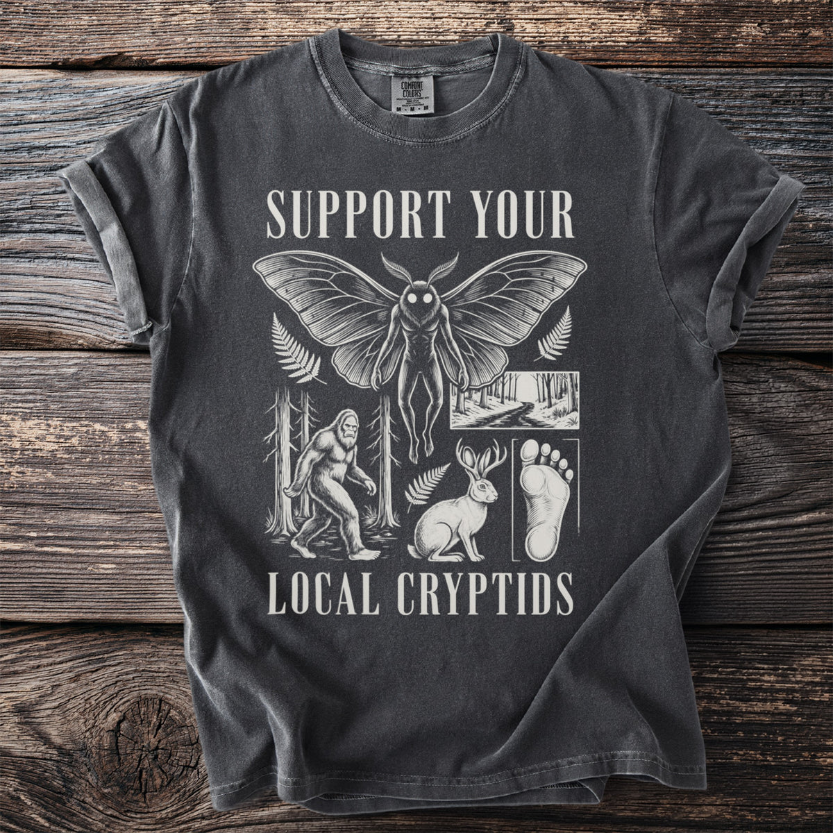 T-shirt graphic with "Support Your Local Cryptids" text and illustrations of Mothman, Bigfoot, rabbit, and footprint.