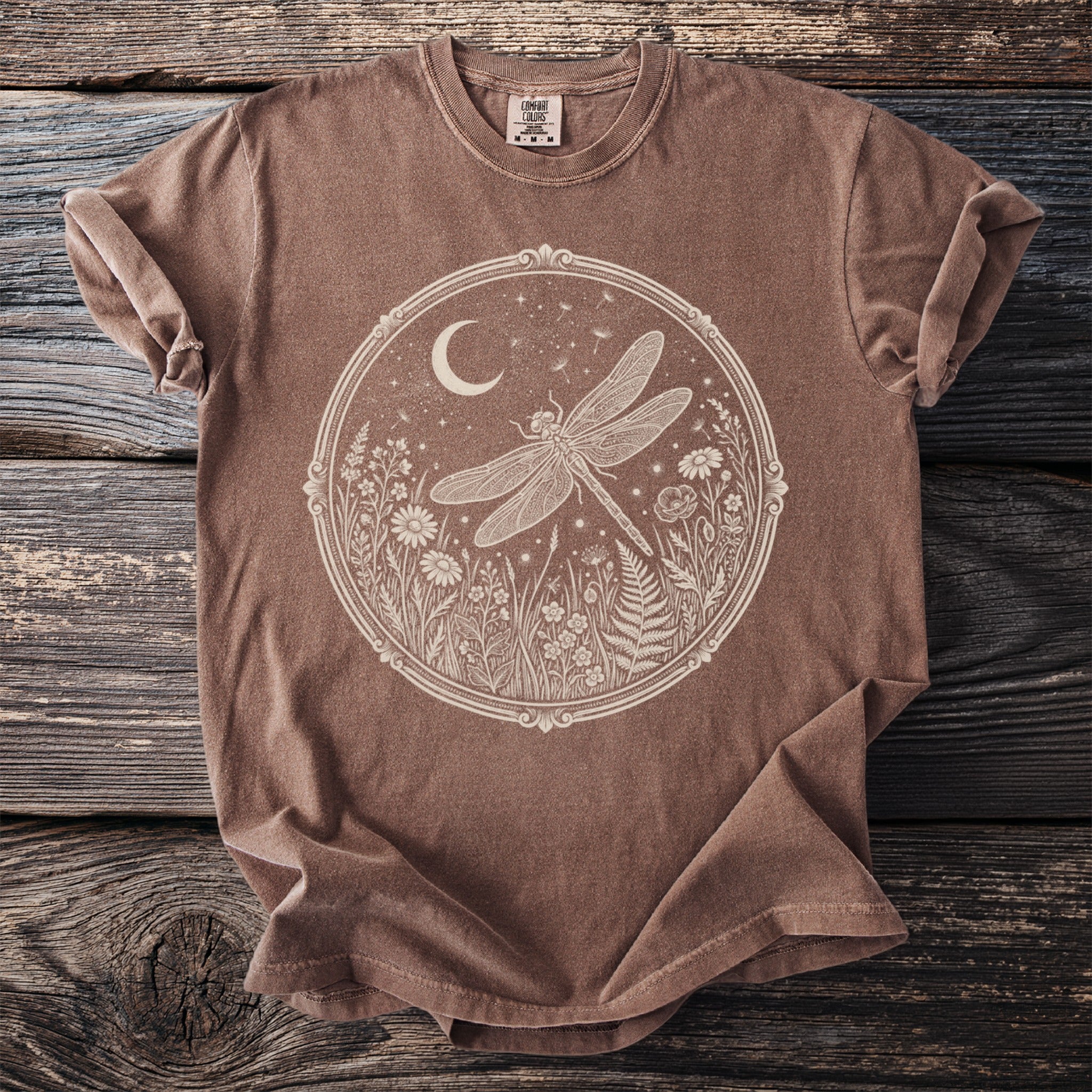 Brown t-shirt with a circular cream graphic of a dragonfly and floral elements.