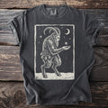 Pepper gray t-shirt with a cream folk-cut print: Krampus stands in the snow, chains and bells on, holding out one hand for a falling snowflake.