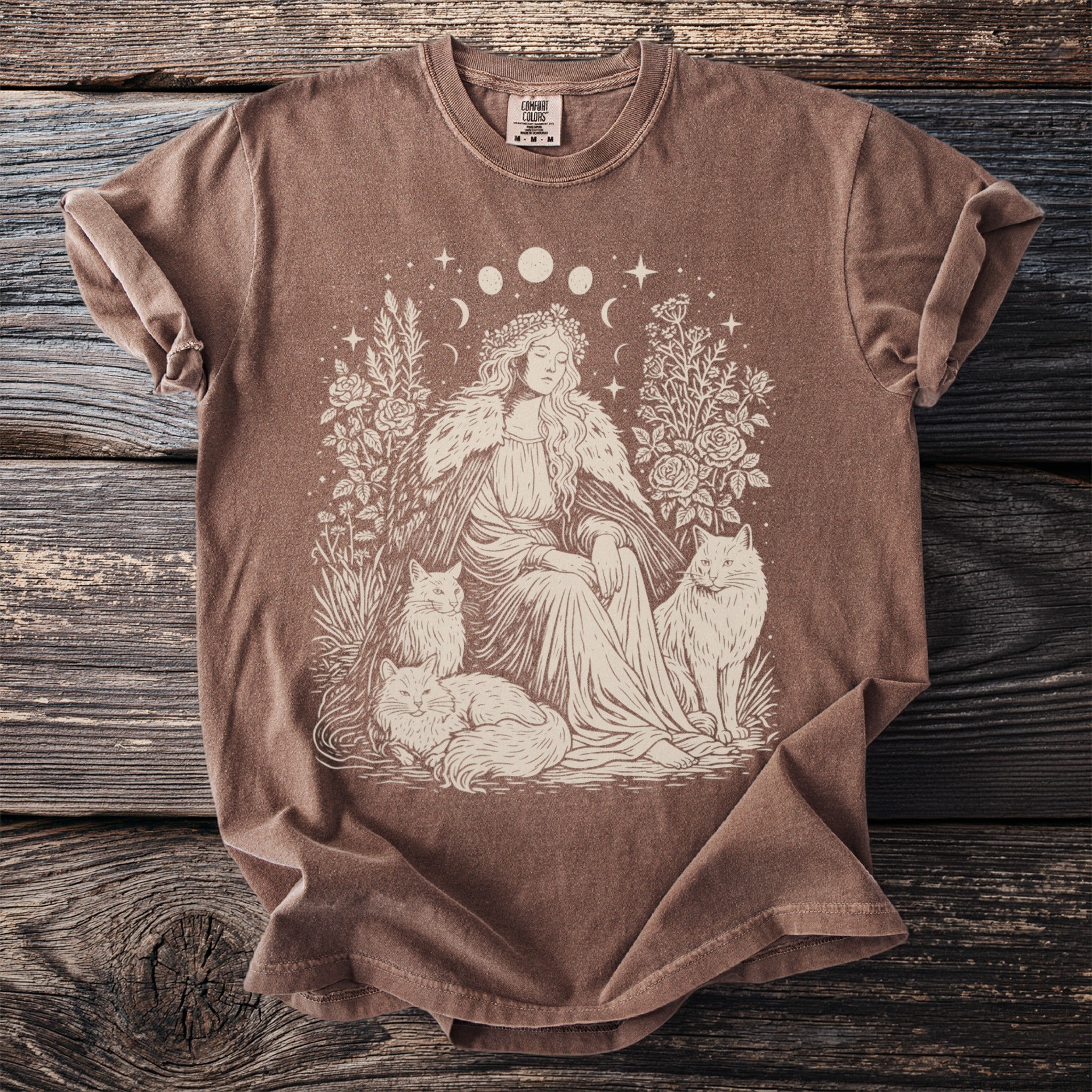 Brown t-shirt with illustration of woman in flower crown, cats, and moon phases.