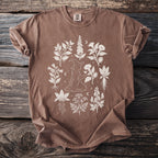 Brown t-shirt with white linework drawing of a witch surrounded by various plants.