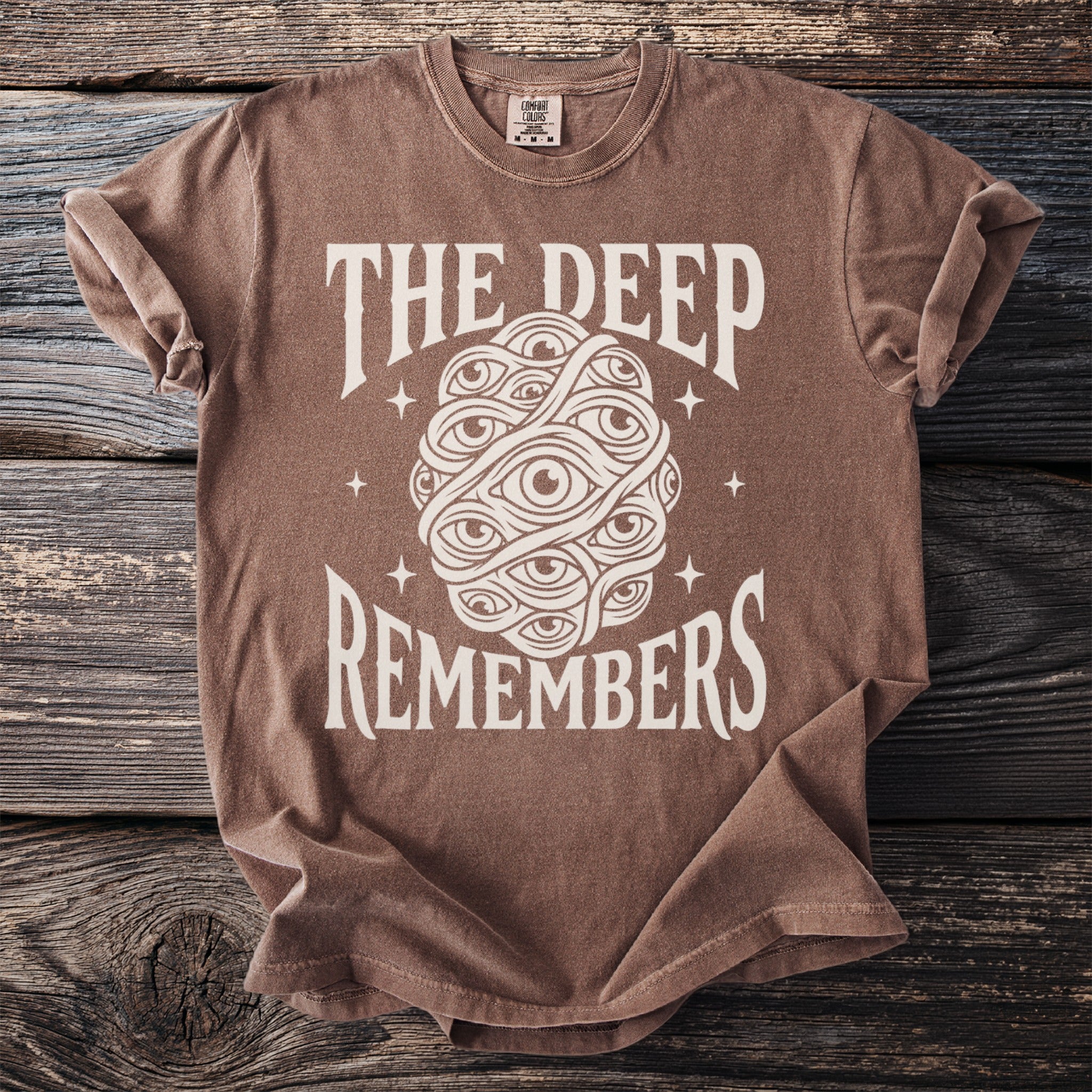 Brown t-shirt with "THE DEEP REMEMBERS" and a cluster of eyes graphic.