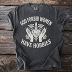 Dark grey t-shirt with white text "GOD FORBID WOMEN HAVE HOBBIES" and graphic.