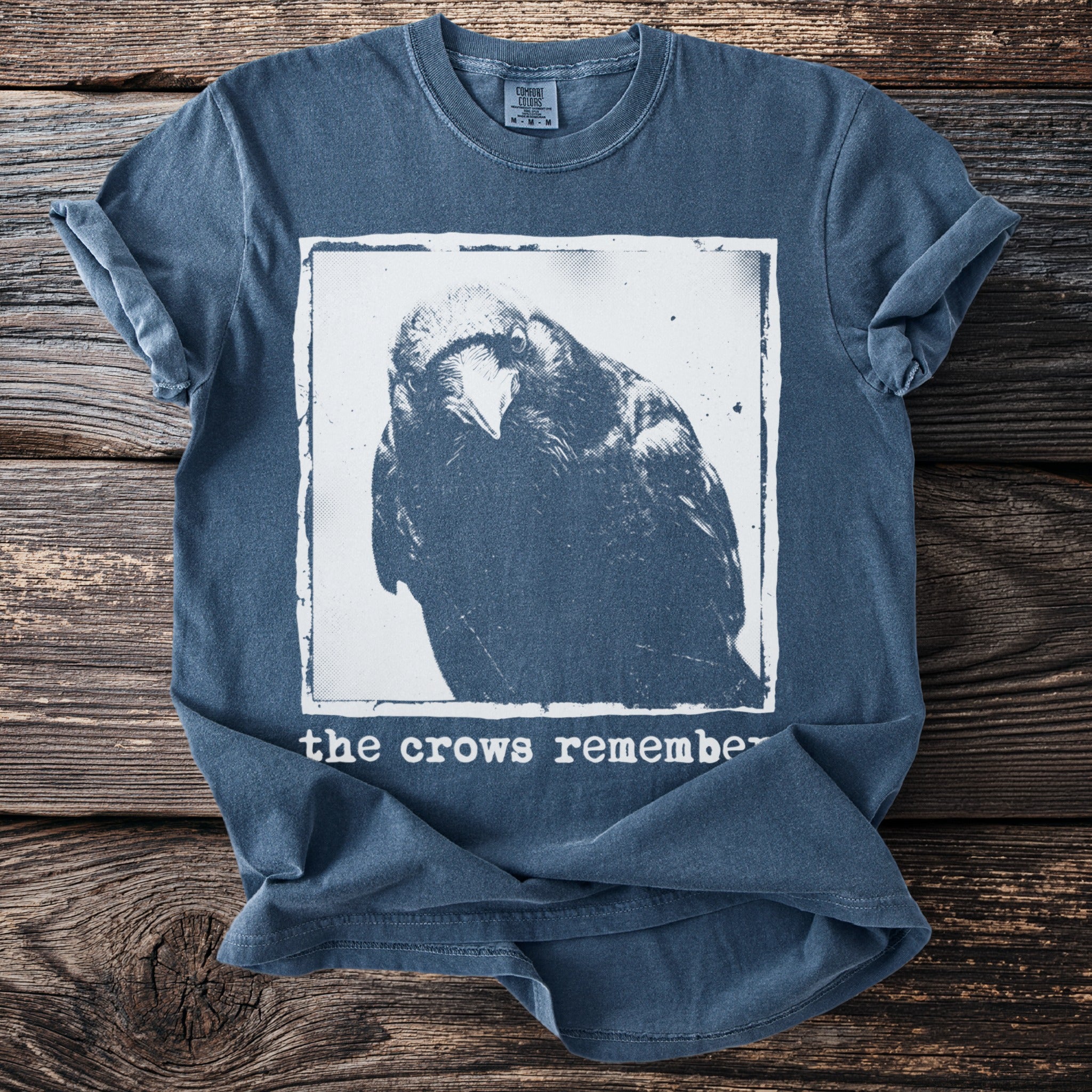 Blue t-shirt with a crow graphic and text reading "the crows remember".