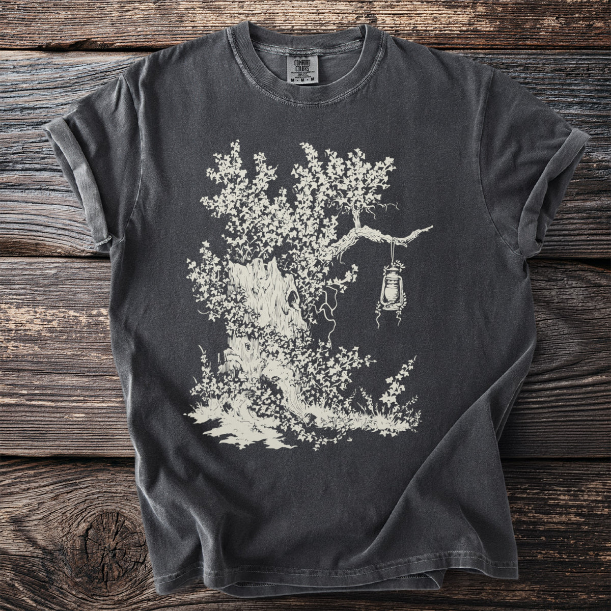 Dark t-shirt with a cream illustration of a gnarled tree with a lantern hanging from a branch.