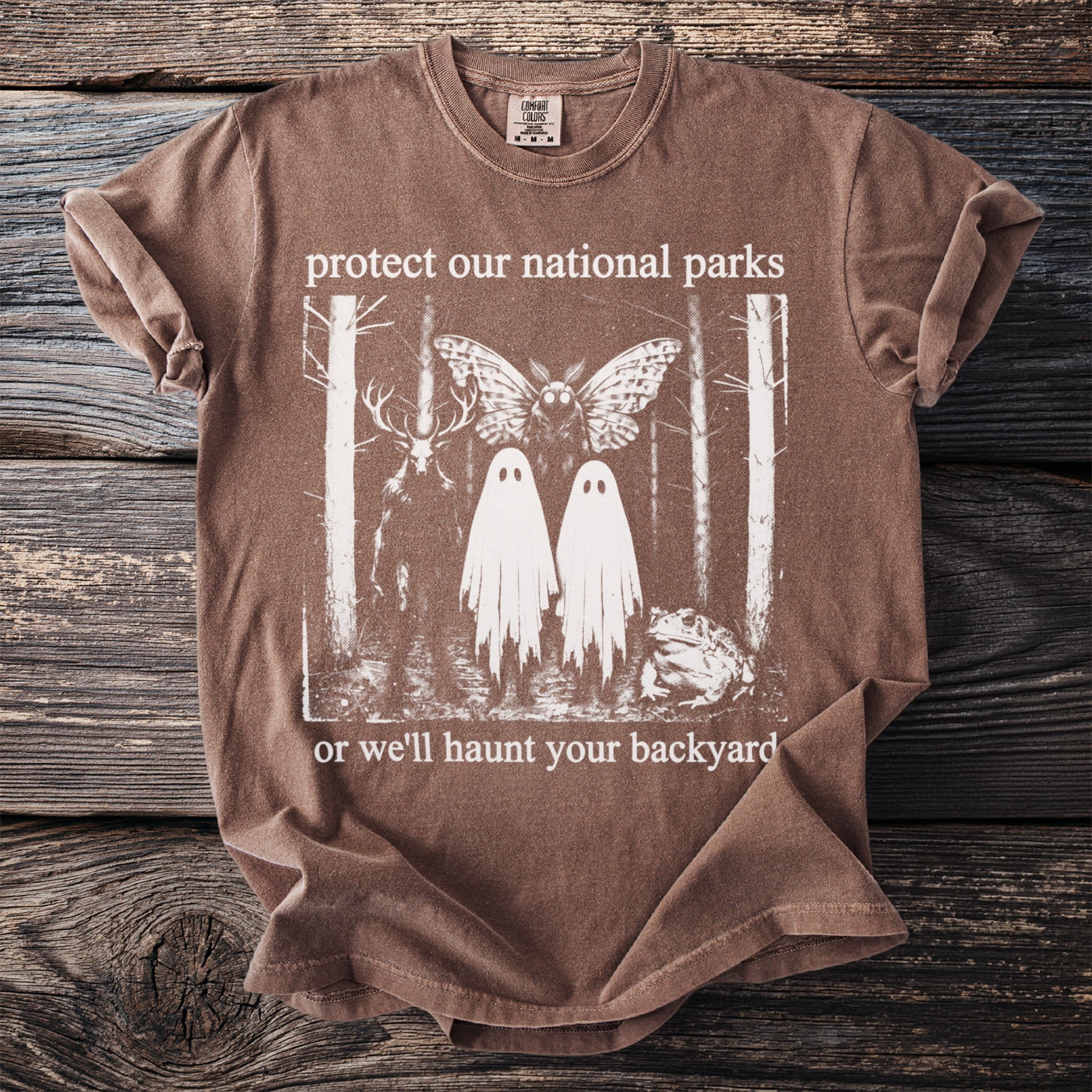 Brown t-shirt with national parks theme artwork: deer, moth, ghosts, and toad.