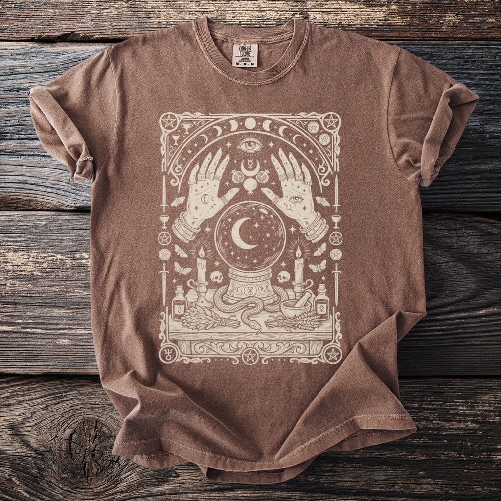Brown t-shirt with cream-colored mystical graphic featuring hands, crystal ball, moon, and celestial elements.