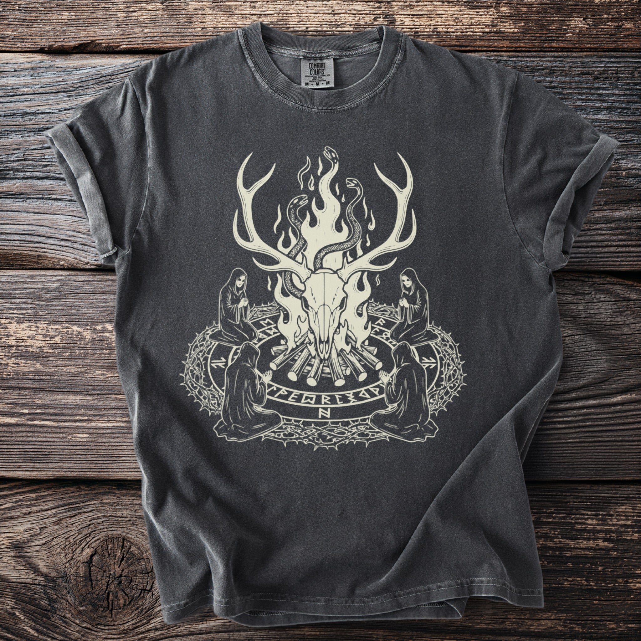 Dark t-shirt with an illustration of a deer skull, snakes, and kneeling figures in a circle.