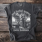 Dark grey t-shirt with "god forbid women have hobbies" text and library illustration.