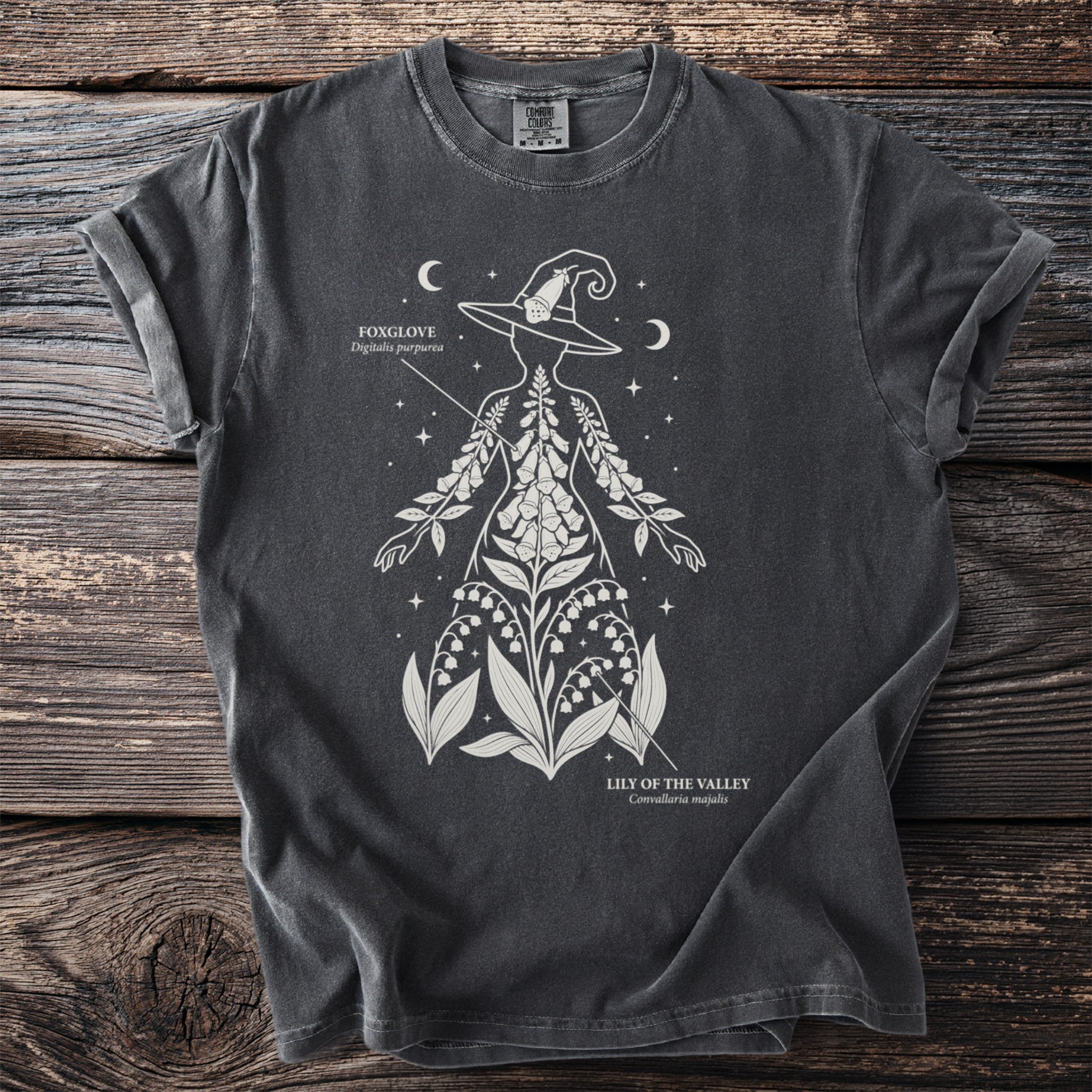 Dark t-shirt with white line art of a witch hat silhouette filled with foxglove and lily of the valley.