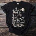 Black t-shirt with cream winged goat on tree and moonlit forest scene.