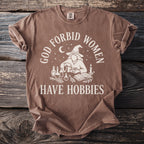Brown t-shirt with cream graphic design that reads "God forbid women have hobbies."