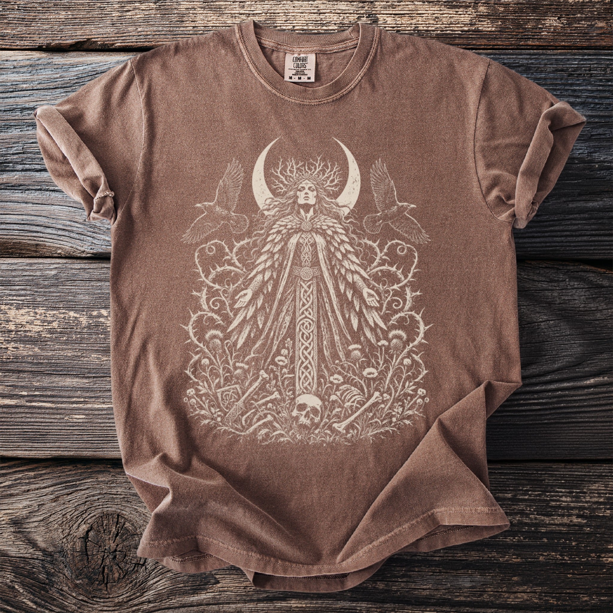 Brown t-shirt with a white graphic of a woman, crescent moon, ravens, and floral elements.