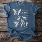 Blue t-shirt with "The Cryptid Field Guide" design featuring Mothman, Loch Ness Monster, Jackalope, Chupacabra, Jersey Devil, and Sasquatch.