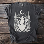 Dark t-shirt with a white silhouette of a meditating witch, moon, stars, and botanical elements.