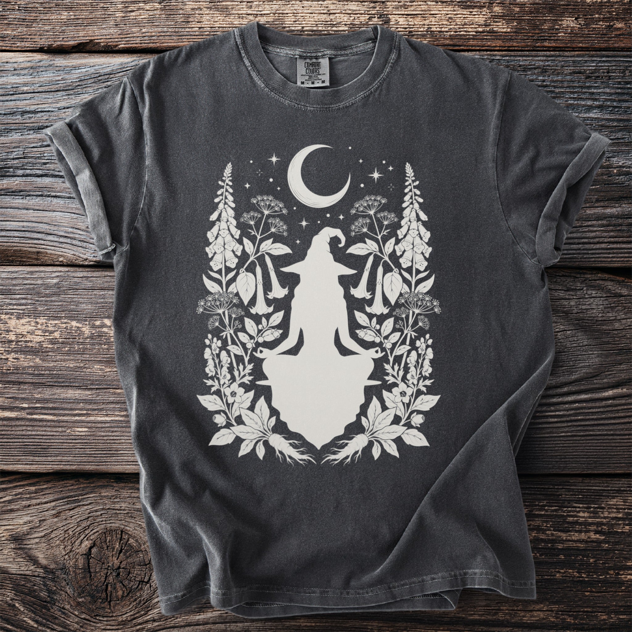 Dark t-shirt with a white silhouette of a meditating witch, moon, stars, and botanical elements.